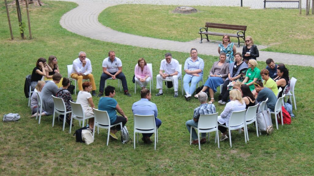 Large group seated in a circle of chairs during an outdoor group recovery meeting