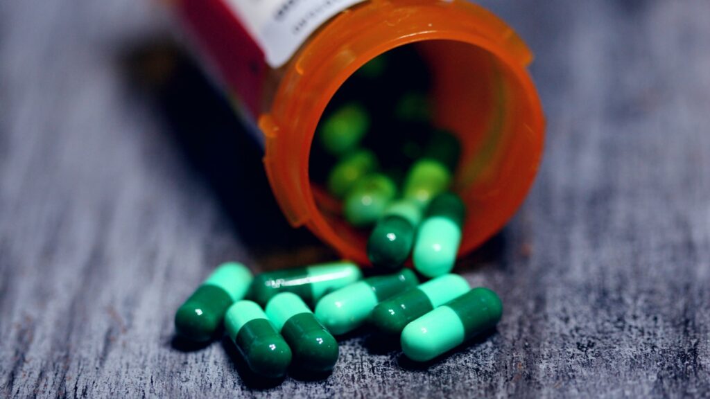 Green capsules spilling from an orange prescription pill bottle