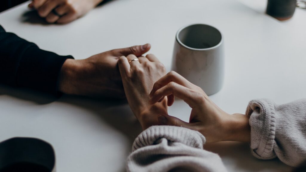 Two people holding hands across a table beside a mug of coffee