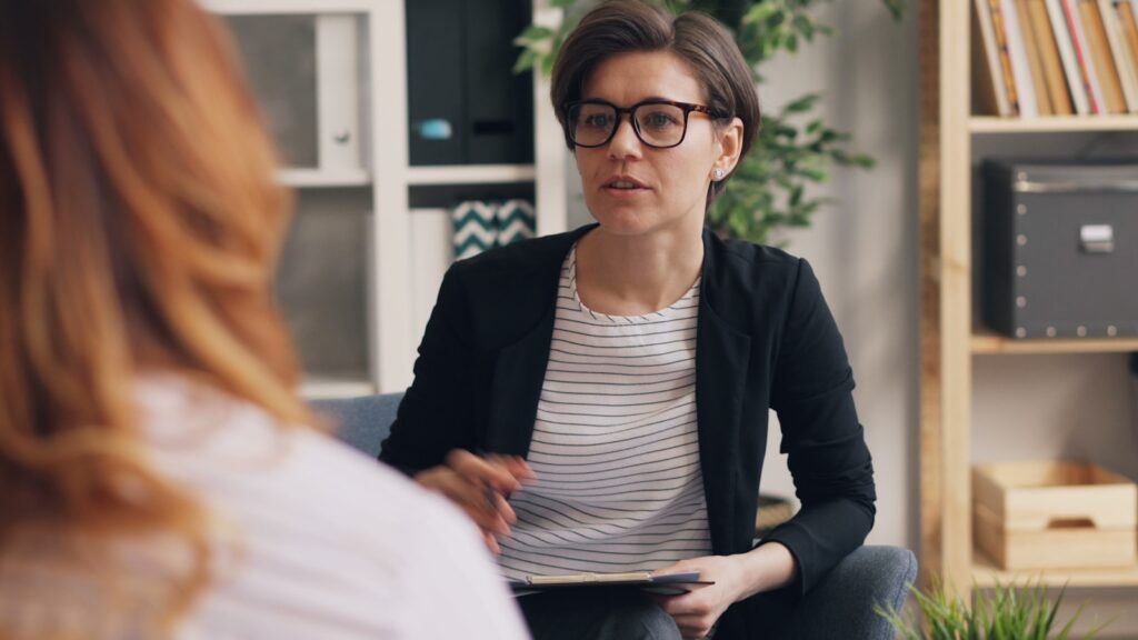 Therapist taking notes while a client speaks during a PTSD therapy session