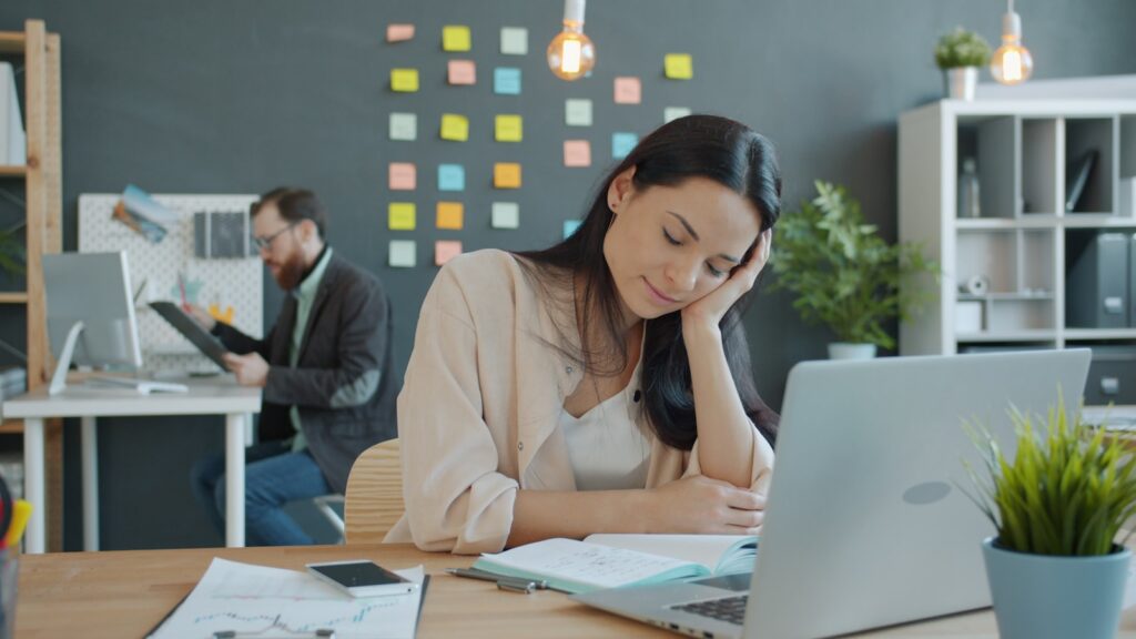 Employee resting her head on her hand at an office desk showing workplace strain
